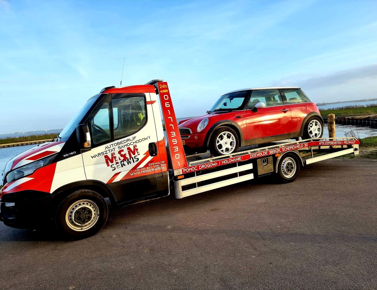 Iveco bergingswagen met een rode Mini op de laadbak bij zonsondergang